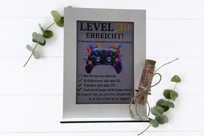 Bilderrahmen „Level erreicht“ mit Geldröhrchen als Geburtstagsgeschenk – frontal fotografiert

