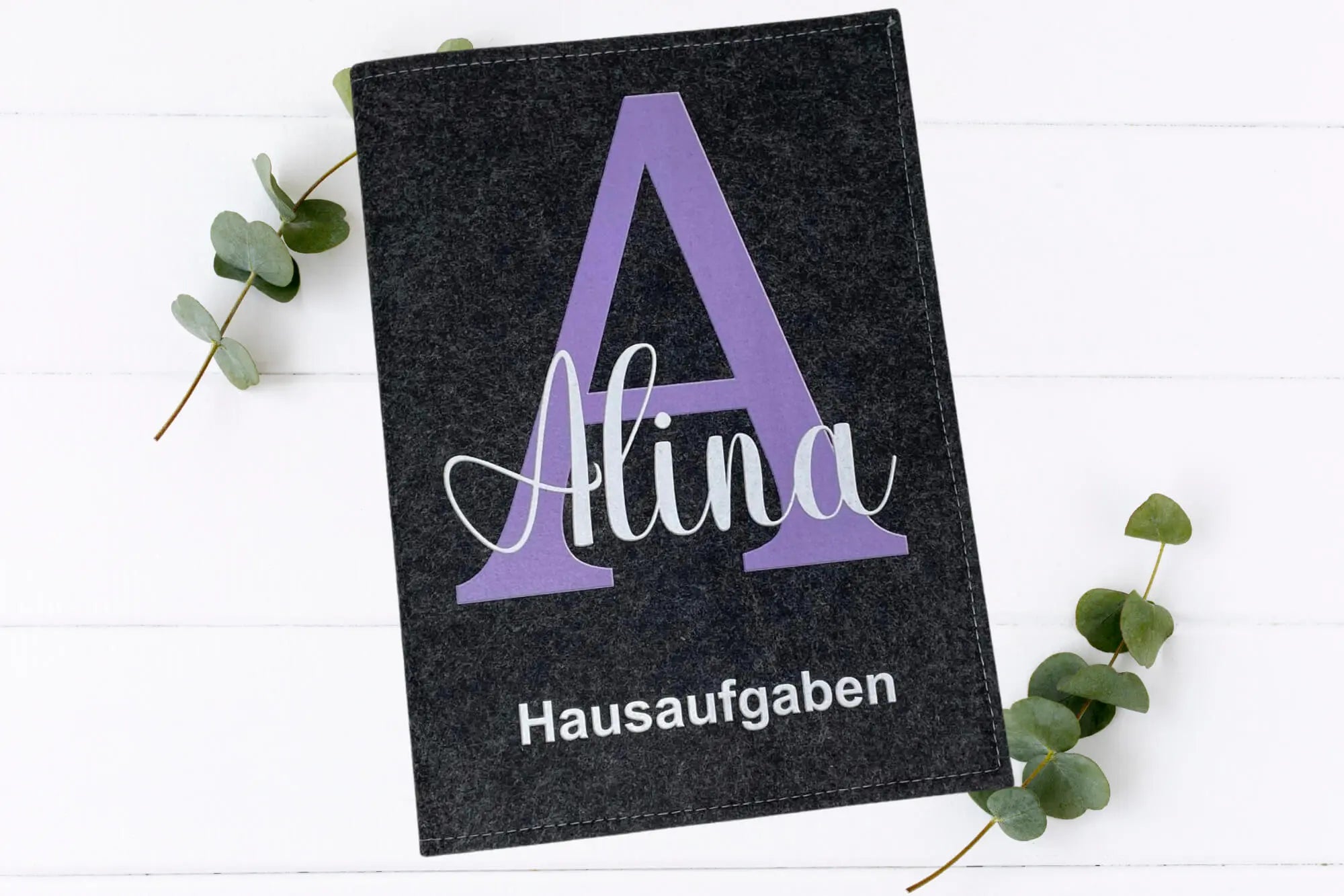 Design-Hüllen für Schulhefte mit dekorativem Anfangsbuchstaben und der Aufschrift „Hausaufgaben“.