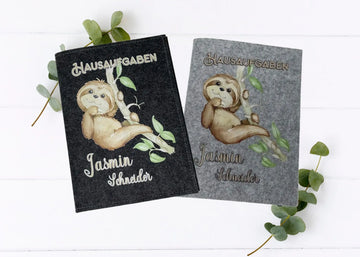 Zwei Filzhüllen für Hausaufgabenhefte mit niedlichem Faultier auf Ast, in Dunkelgrau und Hellgrau.