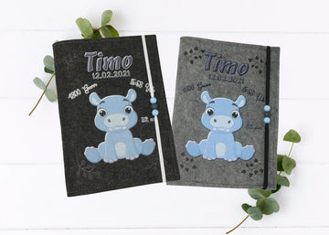 Personalisierte U-Heft-Hülle aus grauem Filz mit süßem blauen Nilpferd und Herzspuren.