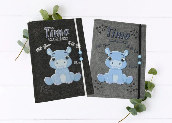 Personalisierte U-Heft-Hülle aus grauem Filz mit süßem blauen Nilpferd und Herzspuren.