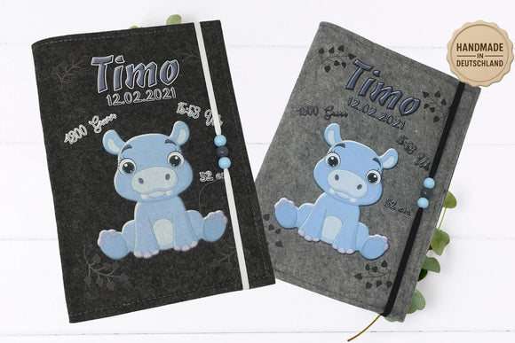 Graue U-Heft-Hülle mit Nilpferdmotiv, liebevollen Details und aufgedruckten Geburtsangaben.