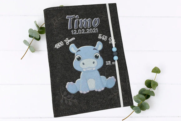 U-Heft-Hülle mit Baby-Hippo und schwarzen Herzspuren, inklusive Platz für Geburtsinformationen.