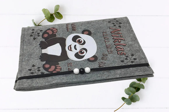 Verspielte U-Heft-Hülle mit sitzendem Panda, rosa Fußsohlen und schwarzen Herzchen auf grauem Filz.