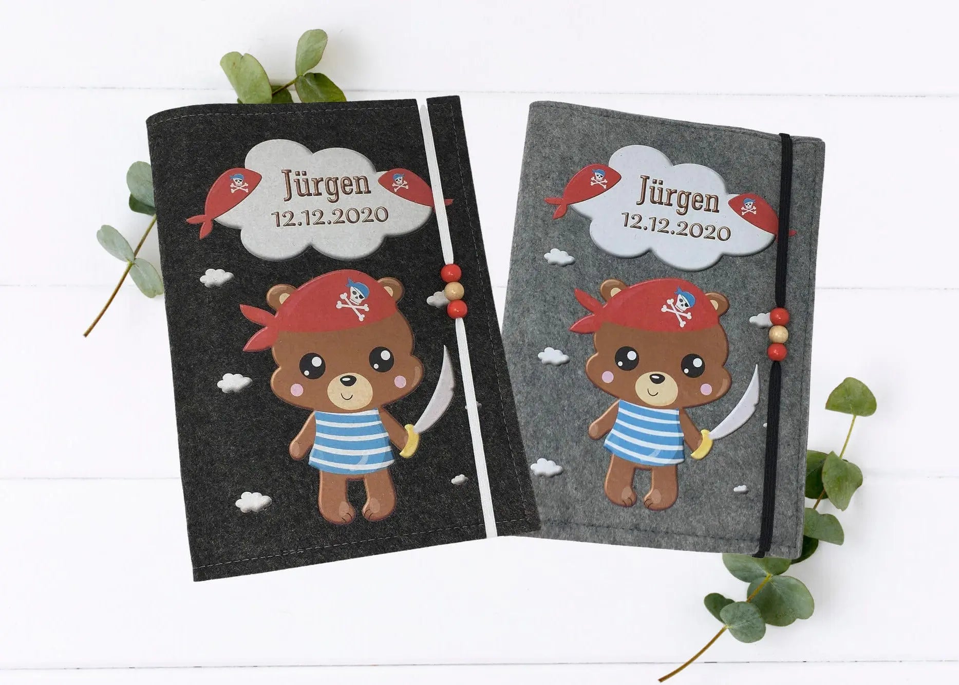Personalisierte U-Heft-Hülle aus grauem Filz mit Piratenbär, rotem Kopftuch und Wolkenmotiv.