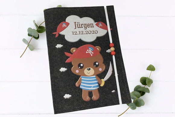 Kindgerechte U-Heft-Hülle mit Piratenmotiv: Bär mit Säbel, Augenklappe und Piratentuch.