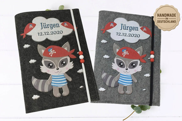 Graue U-Heft-Hülle mit liebevoll gestaltetem Piratenwaschbär in blau-weißem Streifenshirt und Totenkopftuch.