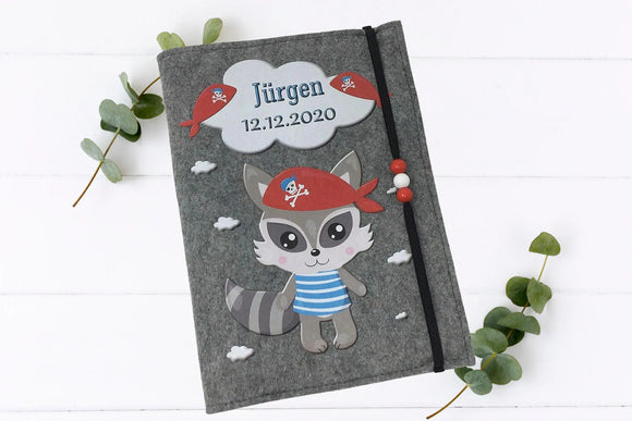 Waschbär mit Piratenmütze und gestreiftem Shirt als Motiv auf einer grauen Filzhülle für das U-Heft.