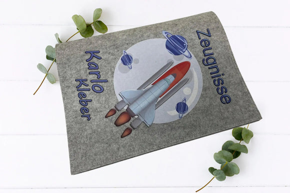 Zeugnismappe mit bunter Rakete, Saturnringen und Weltraumhintergrund – auf Hell- und Dunkelgrau erhältlich