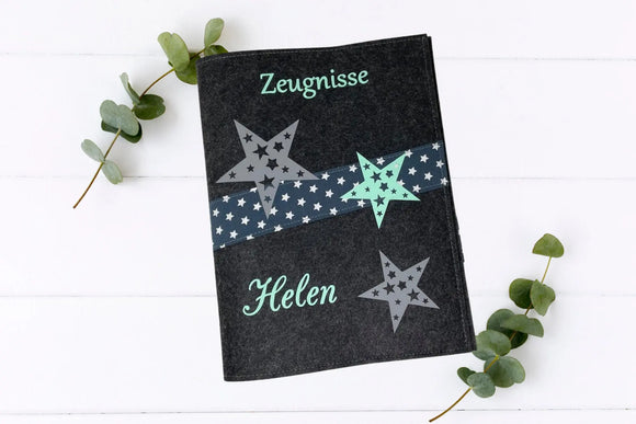 Zeugnismappe aus dunkelgrauem Filz mit mintfarbenem Schriftzug, drei Sternen und diagonaler Borte mit weißen Sternen