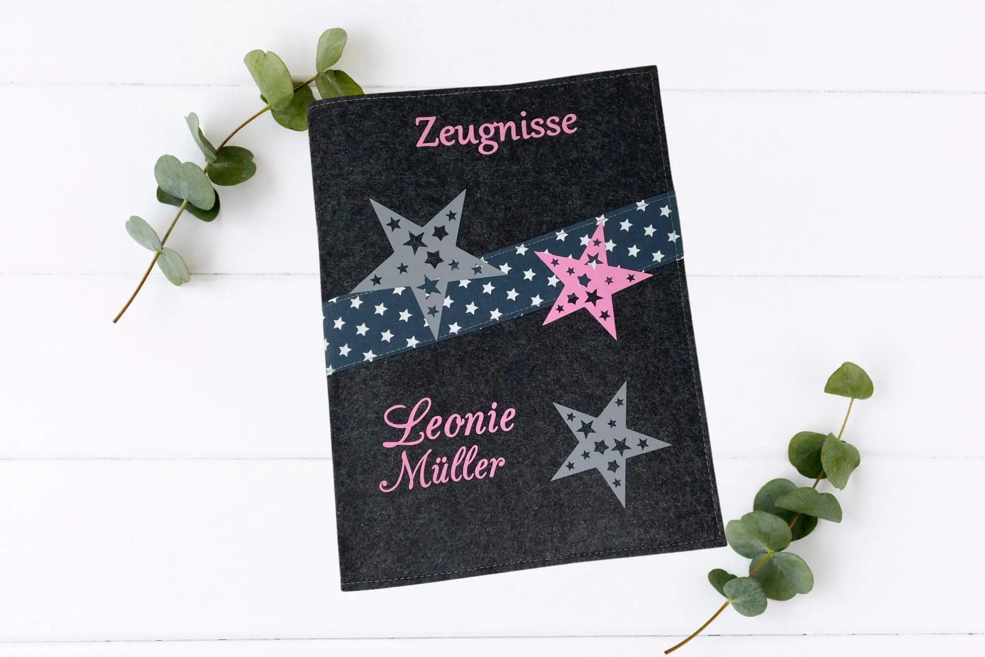 Zeugnismappe aus dunkelgrauem Filz mit mintfarbenem Schriftzug, drei Sternen und diagonaler Borte mit weißen Sternen