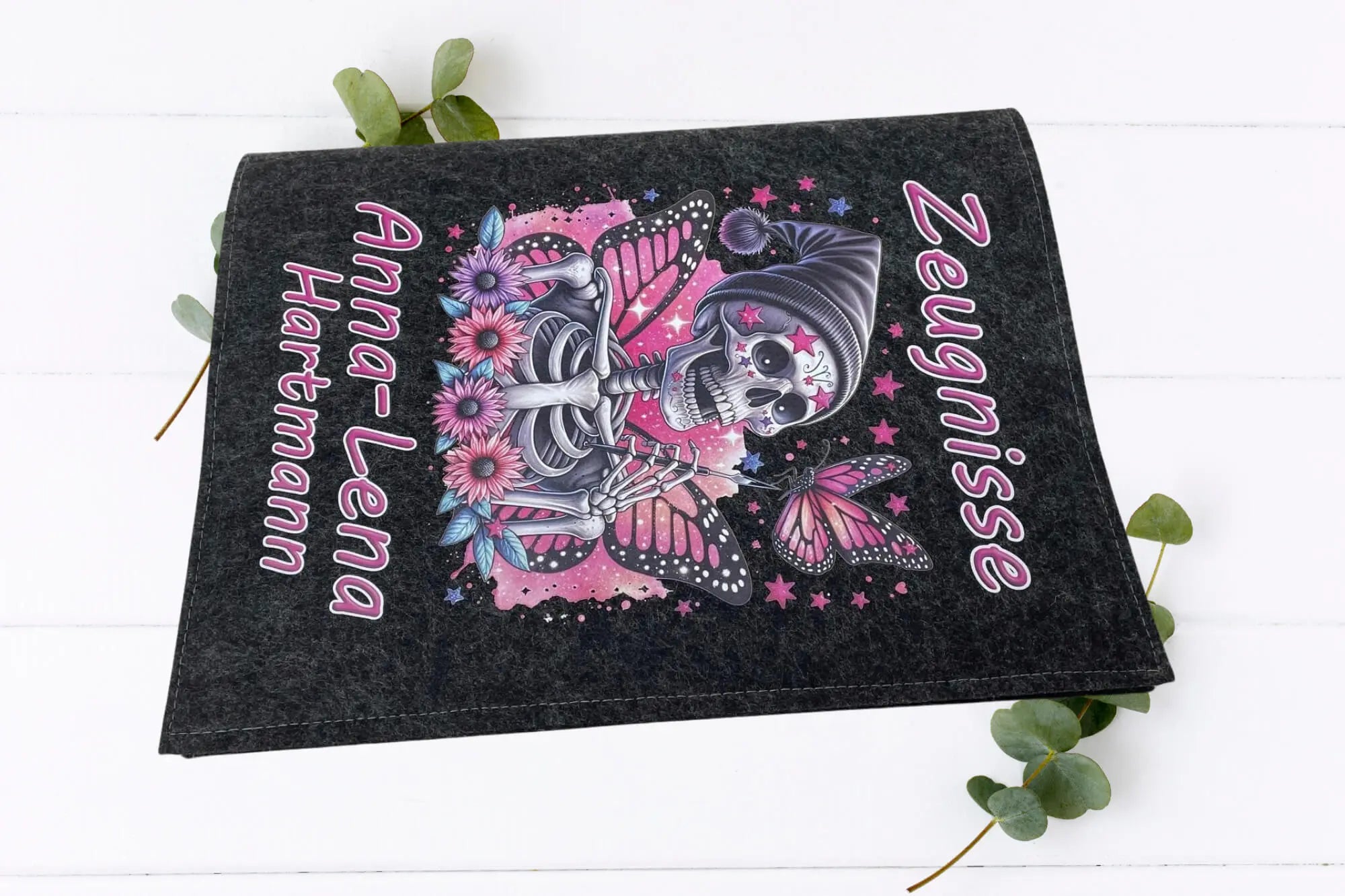 Coole Filz-Zeugnismappe für Mädchen mit personalisiertem Namen – Skelett mit Schmetterlingsflügeln, pinken Blumen und Mütze im Fantasy-Stil.