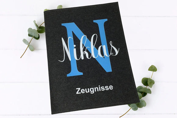 Hochwertige Filzmappe für Schulzeugnisse mit großem Buchstaben-Design und personalisierter Namensaufschrift – in elegantem Schwarz oder Hellgrau.