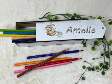 Holz-Stiftebox mit niedlichem Faultier-Motiv, gefüllt mit bunten Buntstiften auf weicher Unterlage