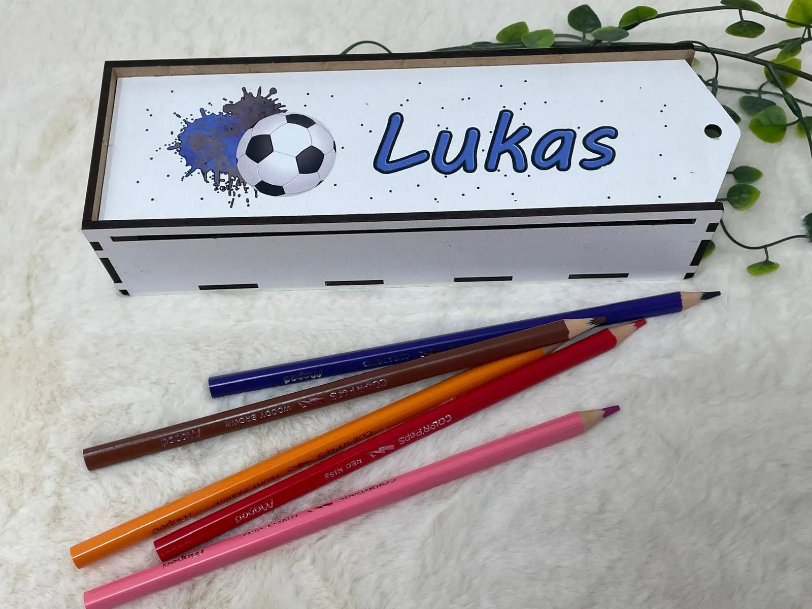 Federmäppchen aus Holz mit blauem Fußball-Design und bunten Stiften auf weicher Unterlage
