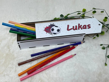 Stiftebox aus Holz mit rotem Fußball-Design und bunten Buntstiften auf weichem Untergrund