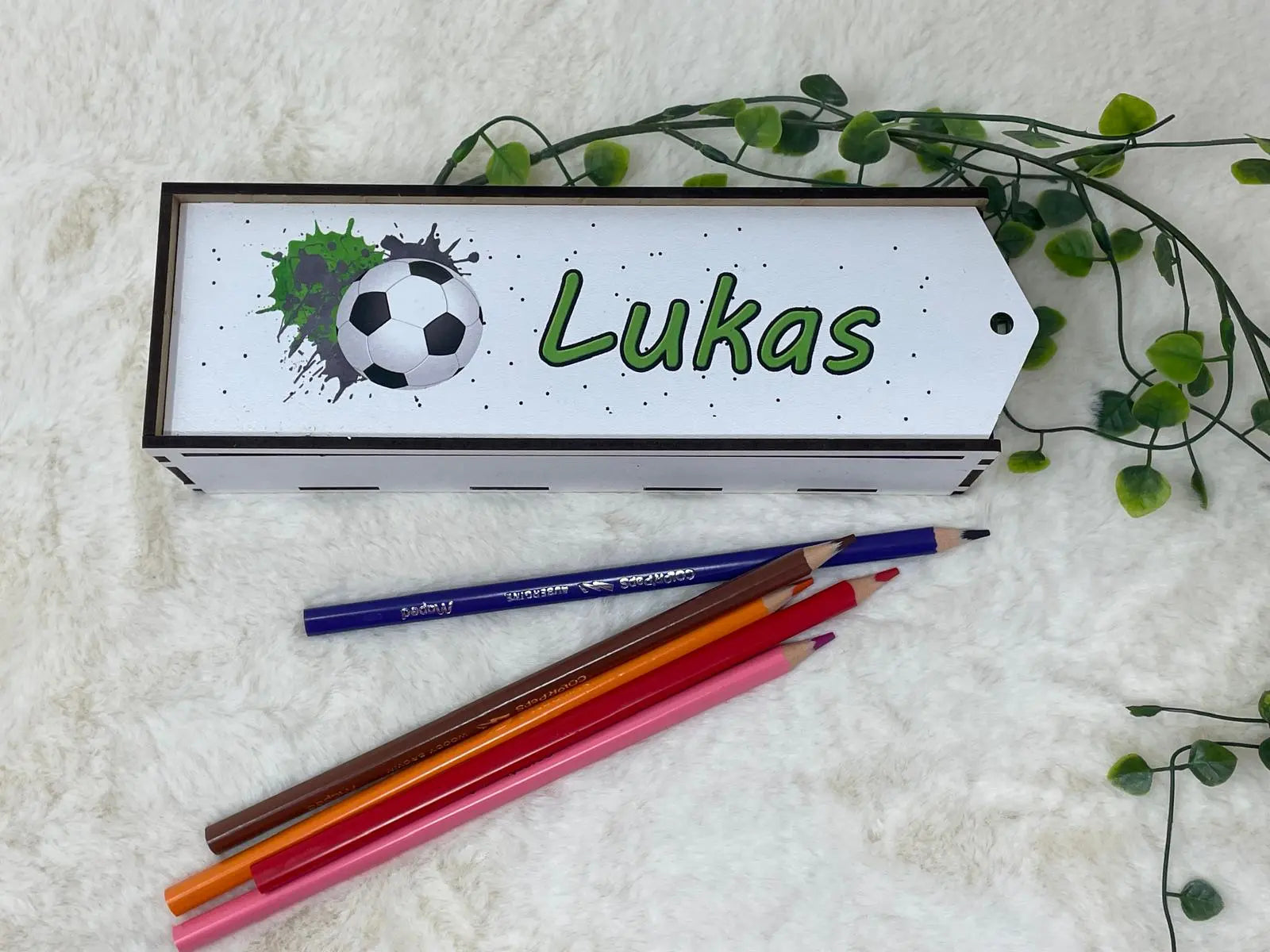 Holzbox für Stifte mit Fußball-Symbol auf weißem Schild, umgeben von bunten Farbstiften