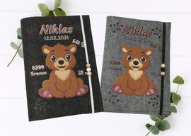 Personalisierte U-Heft-Hülle aus grauem Filz mit fröhlichem Bärenbaby und aufgedruckten Geburtsdaten.