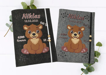 Personalisierte U-Heft-Hülle aus grauem Filz mit fröhlichem Bärenbaby und aufgedruckten Geburtsdaten.