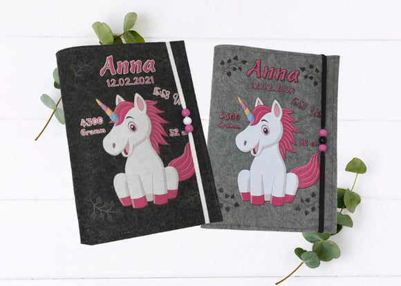 Personalisierte U-Heft-Hülle aus grauem Filz mit fröhlichem Einhornmotiv in Pink und Regenbogenhorn.