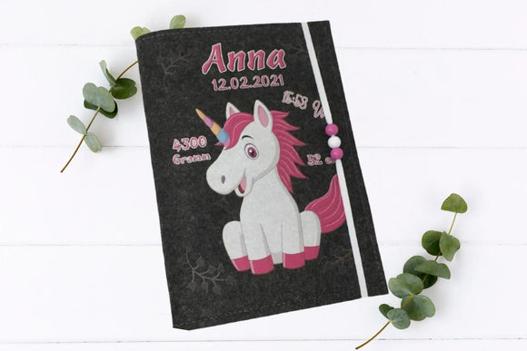 Kindgerechte U-Heft-Hülle mit pinkem Einhorn, schwarzen Herzchen und Gummiband mit bunten Perlen.