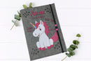 U-Heft-Hülle aus grauem Filz mit Einhorn-Illustration in Weiß und Pink – inkl. Geburtsinformationen.
