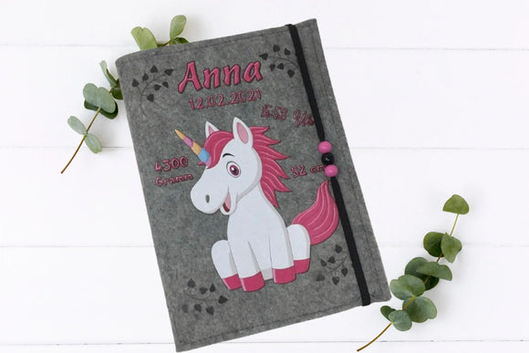 U-Heft-Hülle aus grauem Filz mit Einhorn-Illustration in Weiß und Pink – inkl. Geburtsinformationen.