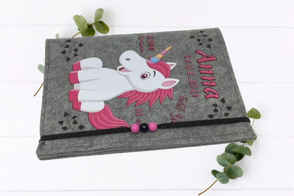 Fröhliches Einhorn mit Regenbogenhorn auf U-Heft-Hülle aus Filz – farbenfroh und personalisierbar.