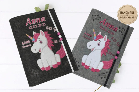 Illustrative Filzhülle mit rosa Einhorn, schwarzen Herzspuren und elastischem Band mit rosa Perlen.