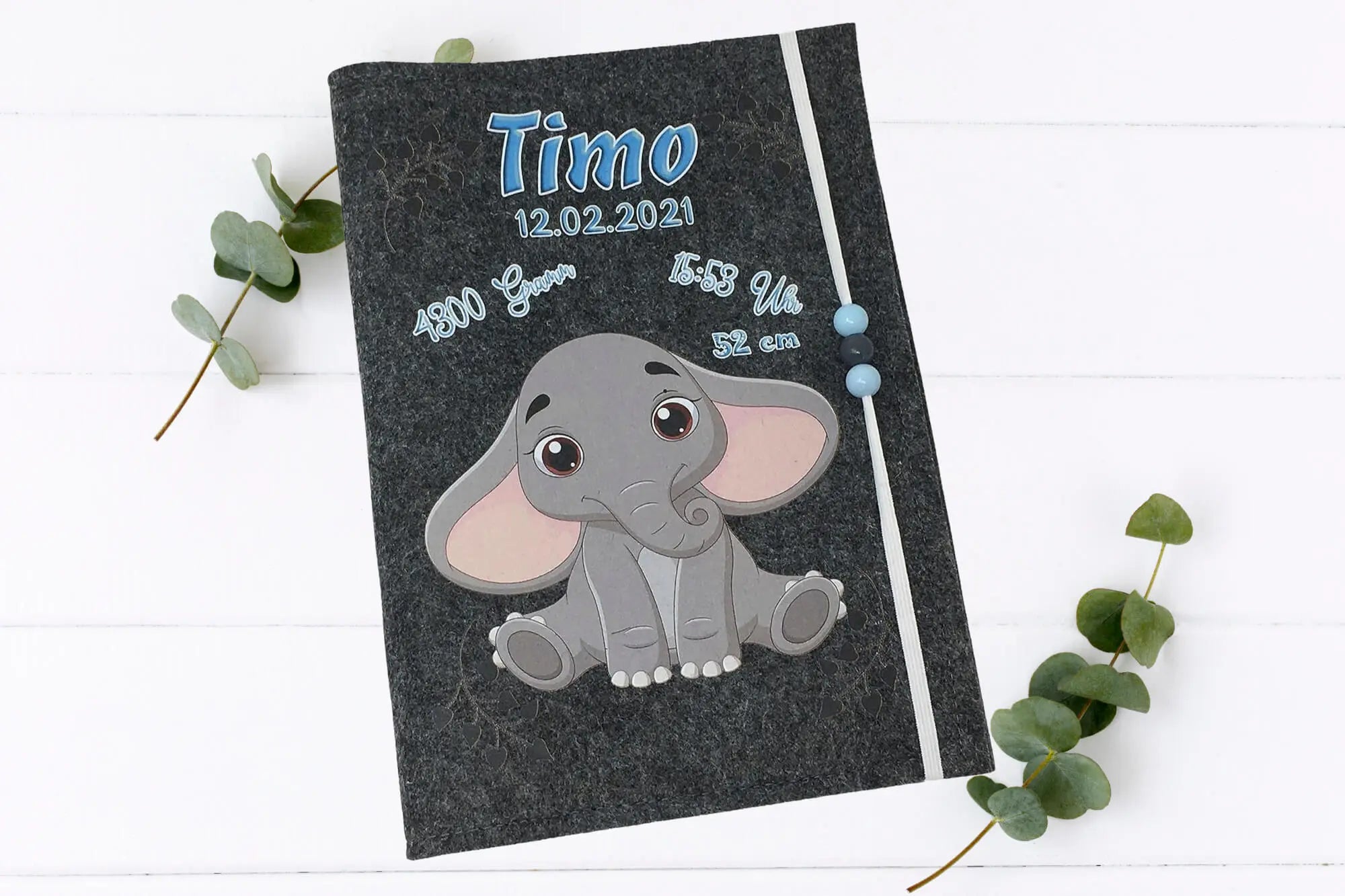 Baby-Elefant mit großen Ohren und braunen Augen auf grauer Filzhülle – liebevolles Geschenk zur Geburt.
