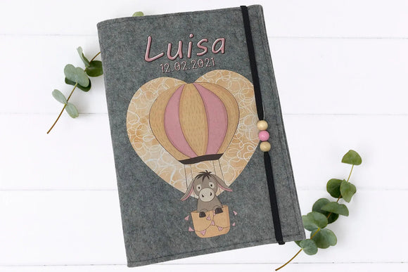 Illustrative U-Heft-Hülle mit fliegendem Esel im Heißluftballon und verspielten Details.