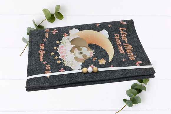Graue Filzhülle mit liebevollem Faultierdesign, rosa Blüten, Halbmond und dekorativen Holzkugeln.