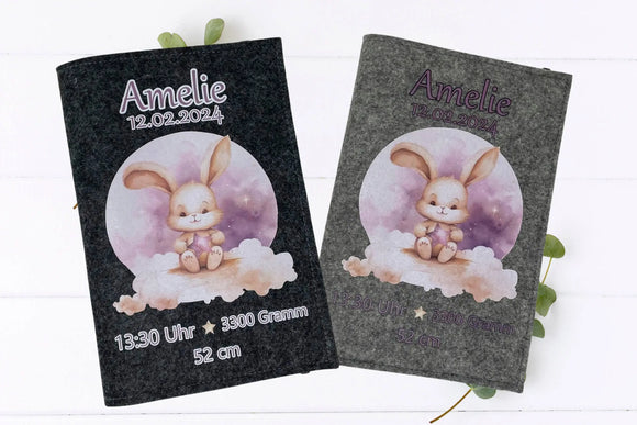 Filzhülle fürs U-Heft mit Aquarell-Hasenmotiv, das einen Stern hält – rosa Himmel und Wolken im Hintergrund