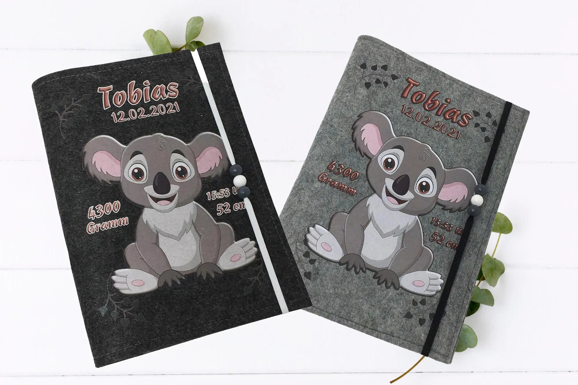 U-Heft-Hülle mit süßem Koala in Grau und Rosa, Herzchen-Spuren und Perlenband zur Fixierung.