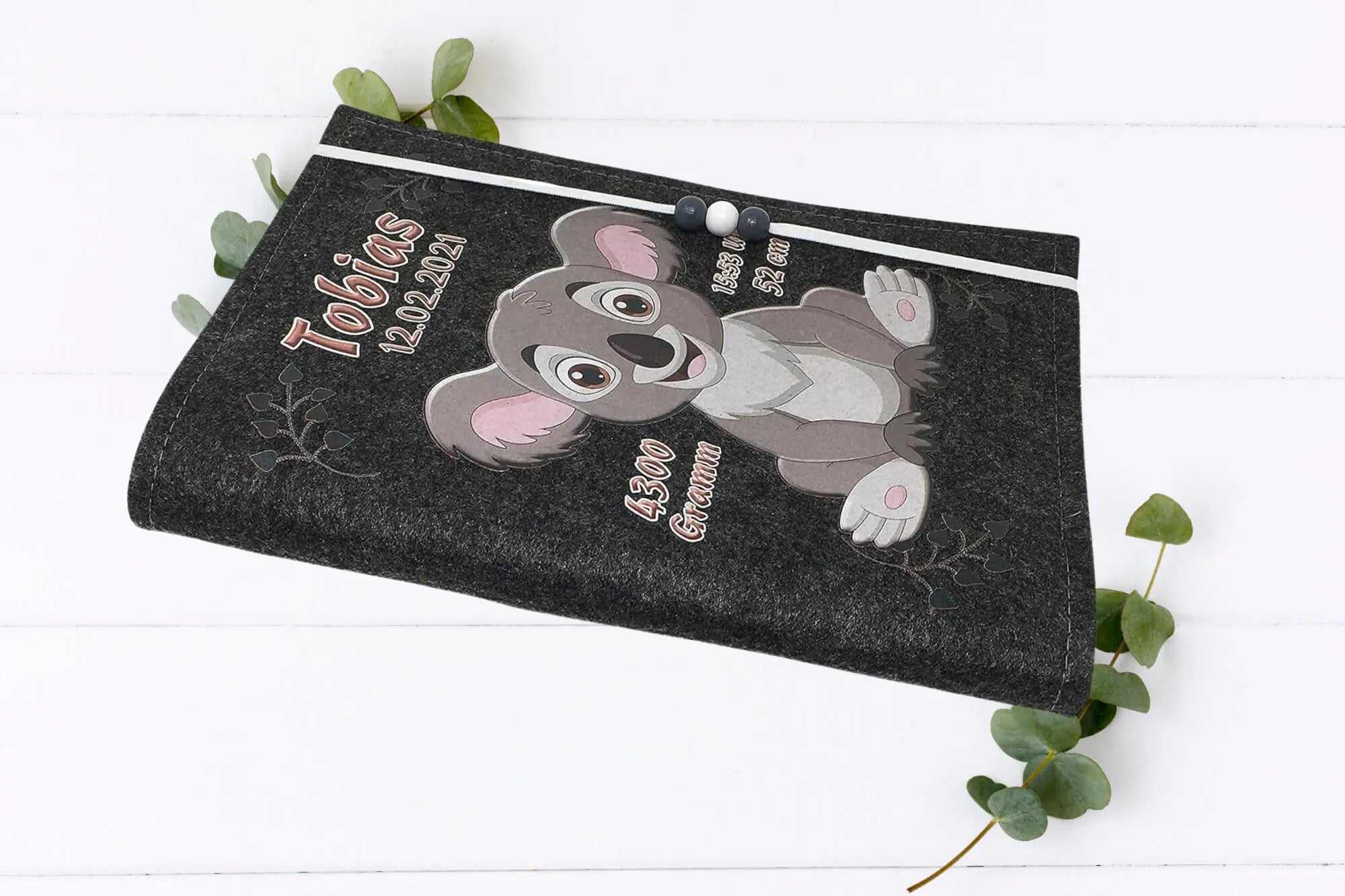 Kindgerechte U-Heft-Hülle mit Koala-Motiv auf grauem Filz und dekorativem Gummiband mit Perlen.