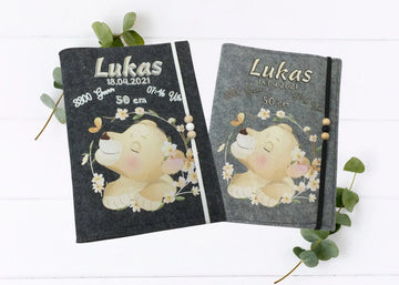 Personalisierte U-Heft-Hülle aus grauem Filz mit schlafendem Löwenbaby und zarten Blumen.