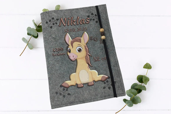 Handgemachte U-Heft-Hülle aus Filz mit braunem Pferd, schwarzen Herzspuren und dekorativen Perlen.