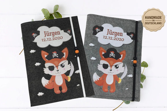Graue Filzhülle fürs U-Heft mit Fuchs in Piratenkleidung, umgeben von kleinen weißen Wolken.