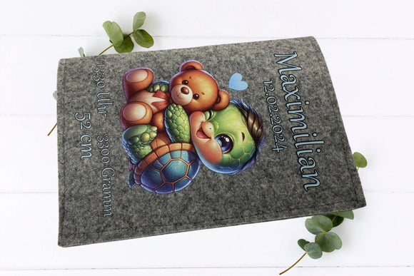 Graue Filzhülle mit Baby-Tier-Motiv: Schildkröte und Teddy in bunter Illustration, ergänzt durch Geburtsdetails.
