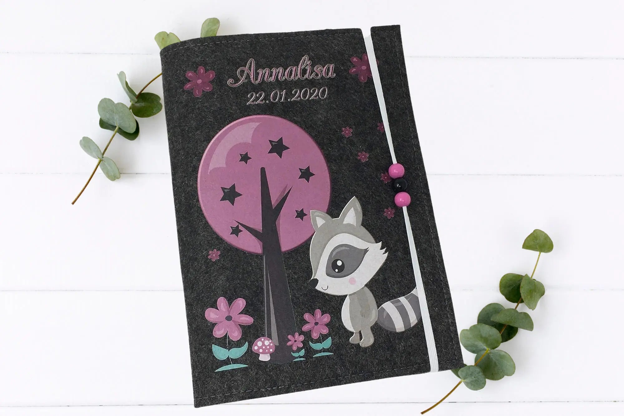 Filzhülle fürs Untersuchungsheft mit Waschbär-Illustration und pink-violettem Naturdesign.