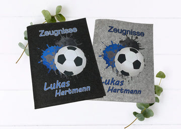 Personalisierte Zeugnismappen aus Filz mit Fußballmotiv und blauen Farbspritzern – mit Namensaufdruck in Hell- und Dunkelgrau.