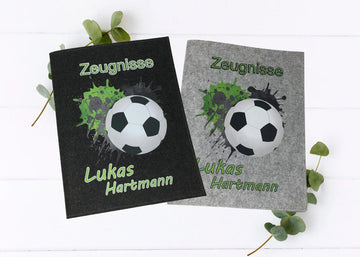 Personalisierte Zeugnismappen aus Filz mit Fußballmotiv und grün-schwarzem Splash-Effekt – mit Name  in Hell- und Dunkelgrau.