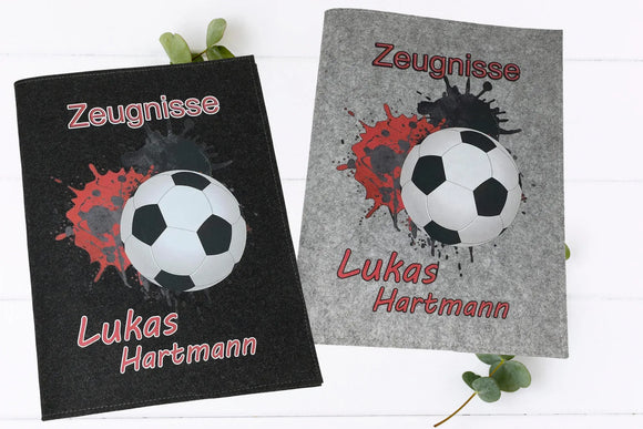 Zeugnismappe Fußball personalisiert – mit Fußball auf Farbspritz-Hintergrund in Dunkelgrau und Hellgrau.