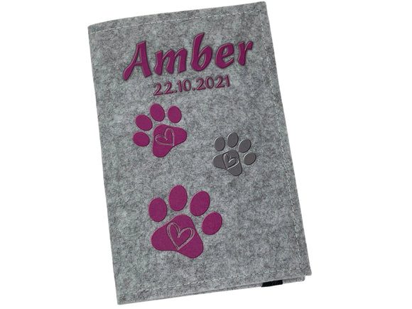 Tierausweishülle aus grauem Filz mit dreifarbigen Pfotenabdrücken und Datum.